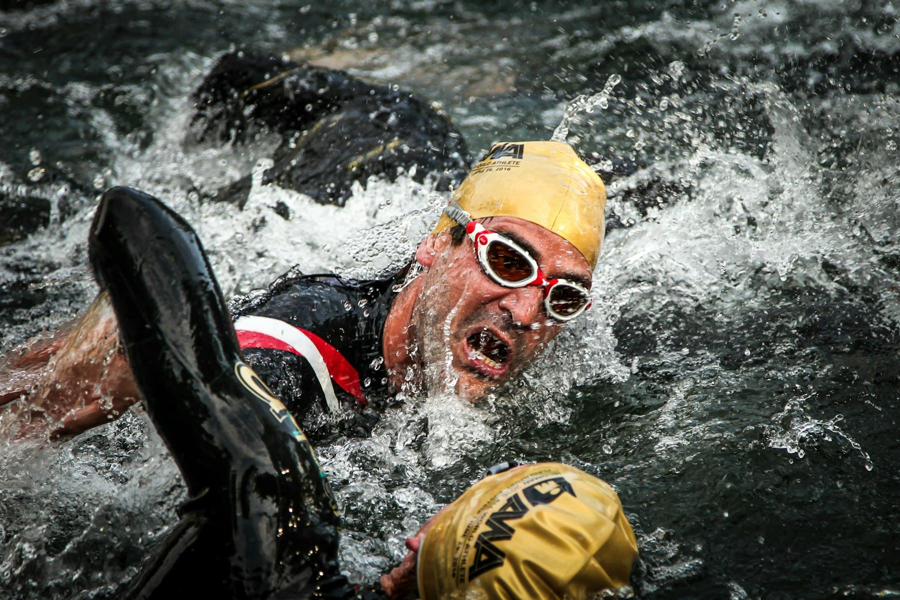 Atleta de touca e óculos nadando crawl na largada de uma prova em mar aberto